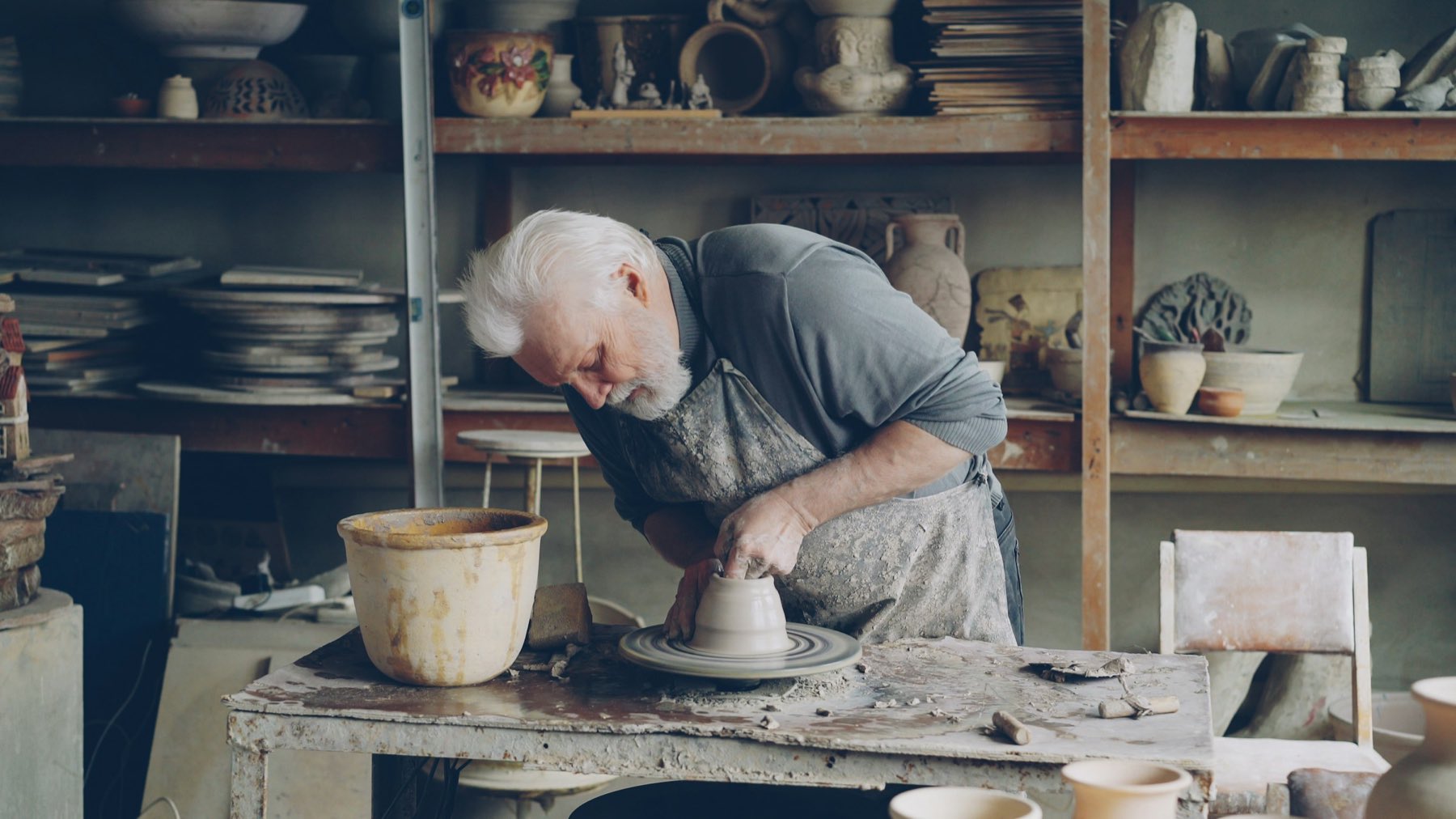 A potter shaping clay on a wheel in a workshop